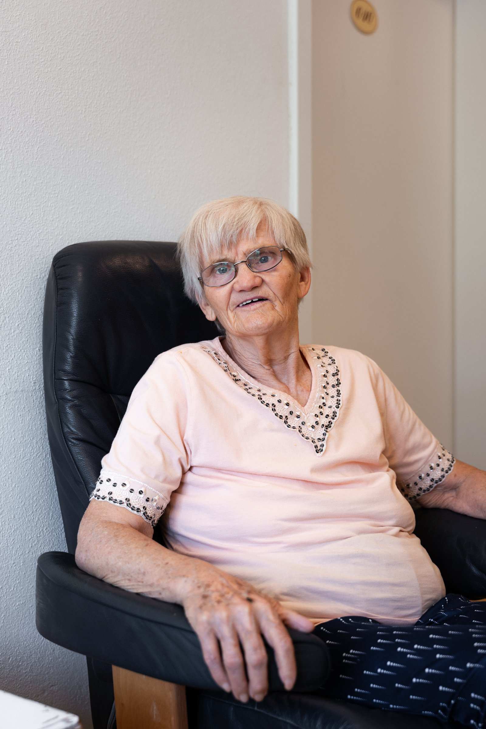 Ältere Bewohnerin sitzt lächelnd in einem Ledersessel
