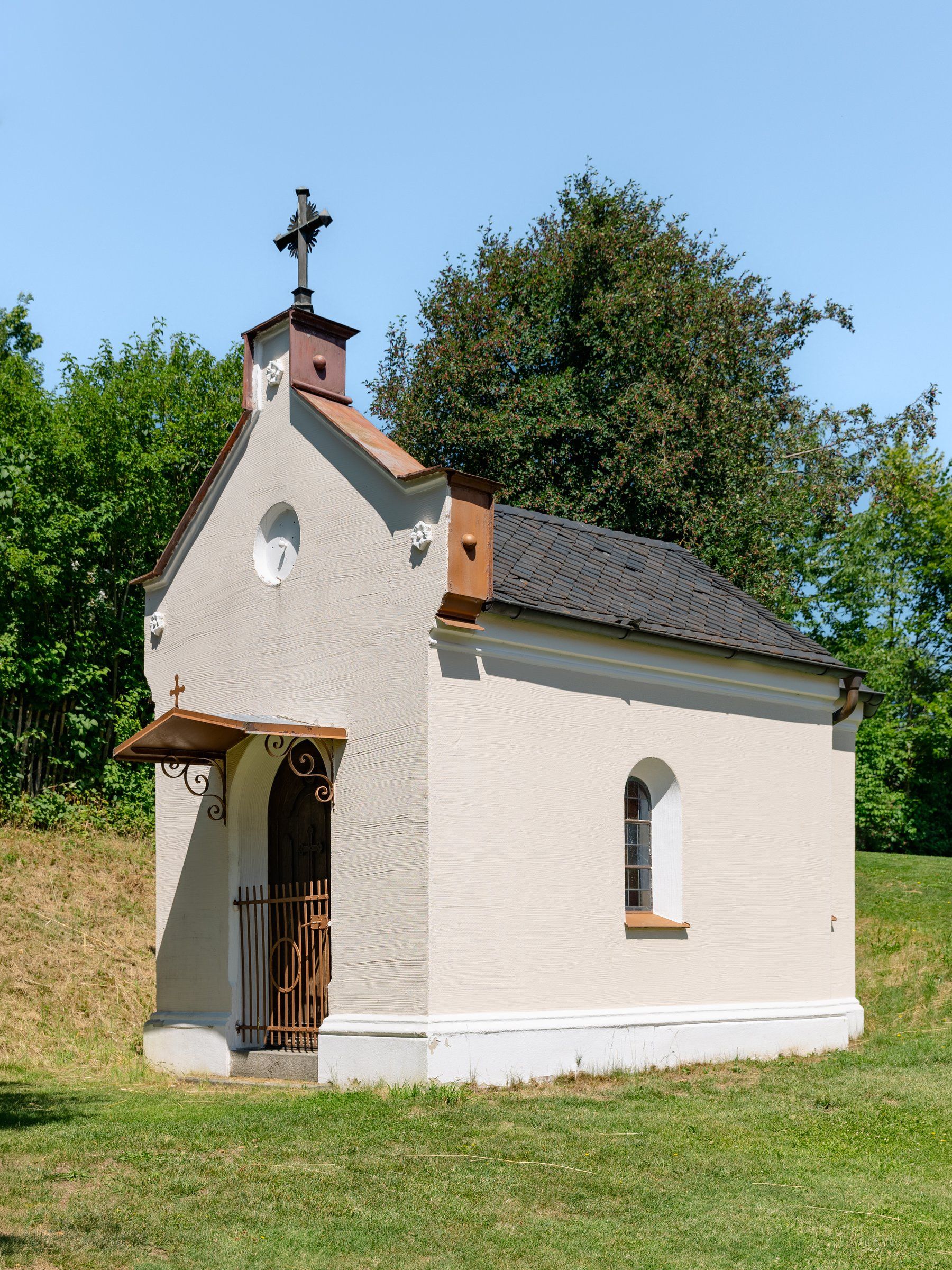 Kleine weiße Kapelle mit Glockentürmchen auf einer Wiese im Garten