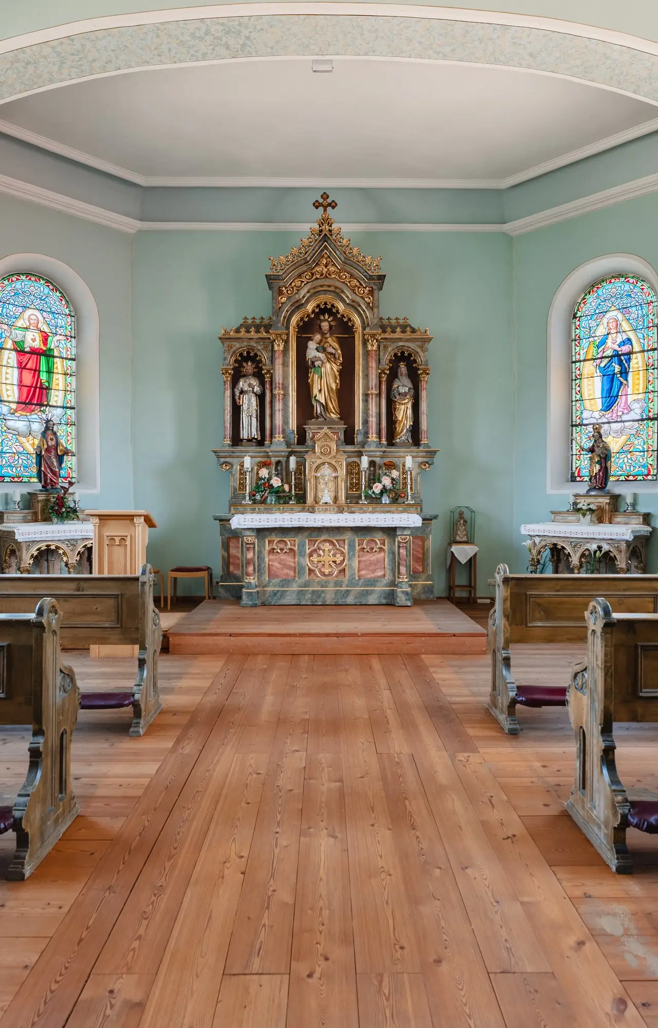 Innenraum der hauseigenen Kapelle mit Holzbänken, vergoldetem Altar und bunten Glasfenstern
