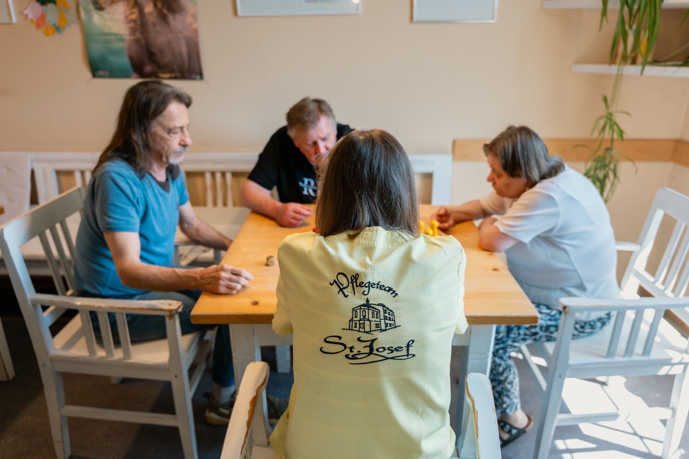 Eine Mitarbeiterin begleitet Bewohner beim gemeinsamen Spiel am Tisch